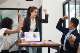 Team steht am Schreibtsch rum und hebt die Hände