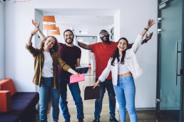 Team steht vor der Kamera energetische Armbewegungen und alle sind happy